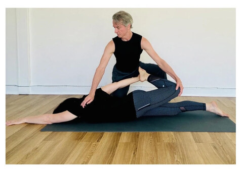 Wayne assists a supine client through a guided leg stretch on the mat.