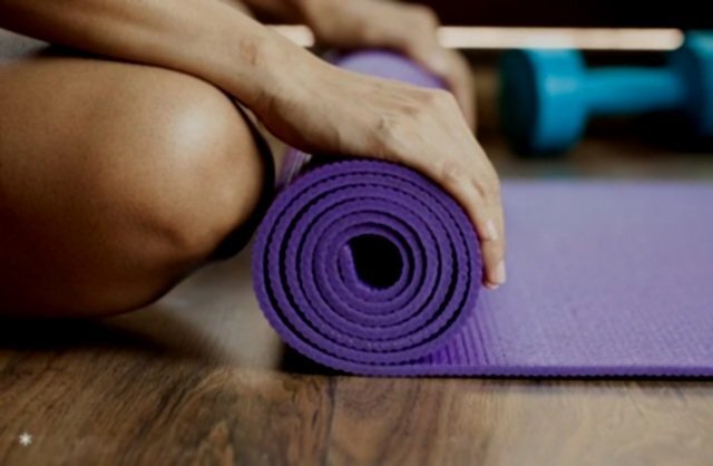 Hands unrolling a purple yoga mat on a wooden studio floor